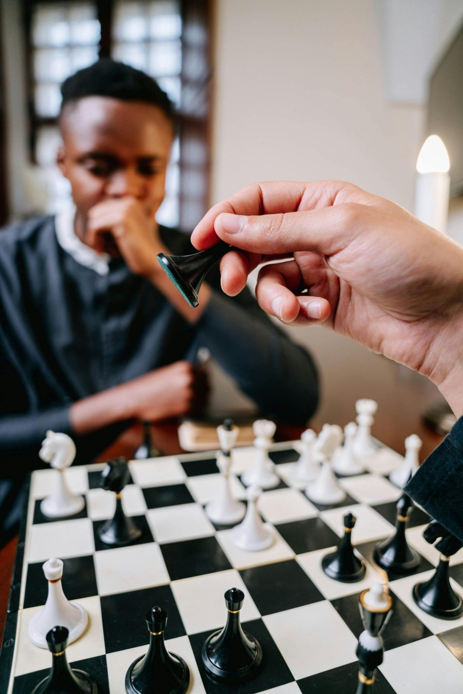 Close-up of hands playing chess, showcasing a strategic move in an indoor setting.