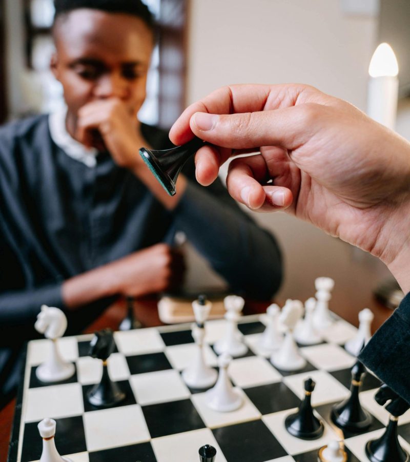 Close-up of hands playing chess, showcasing a strategic move in an indoor setting.